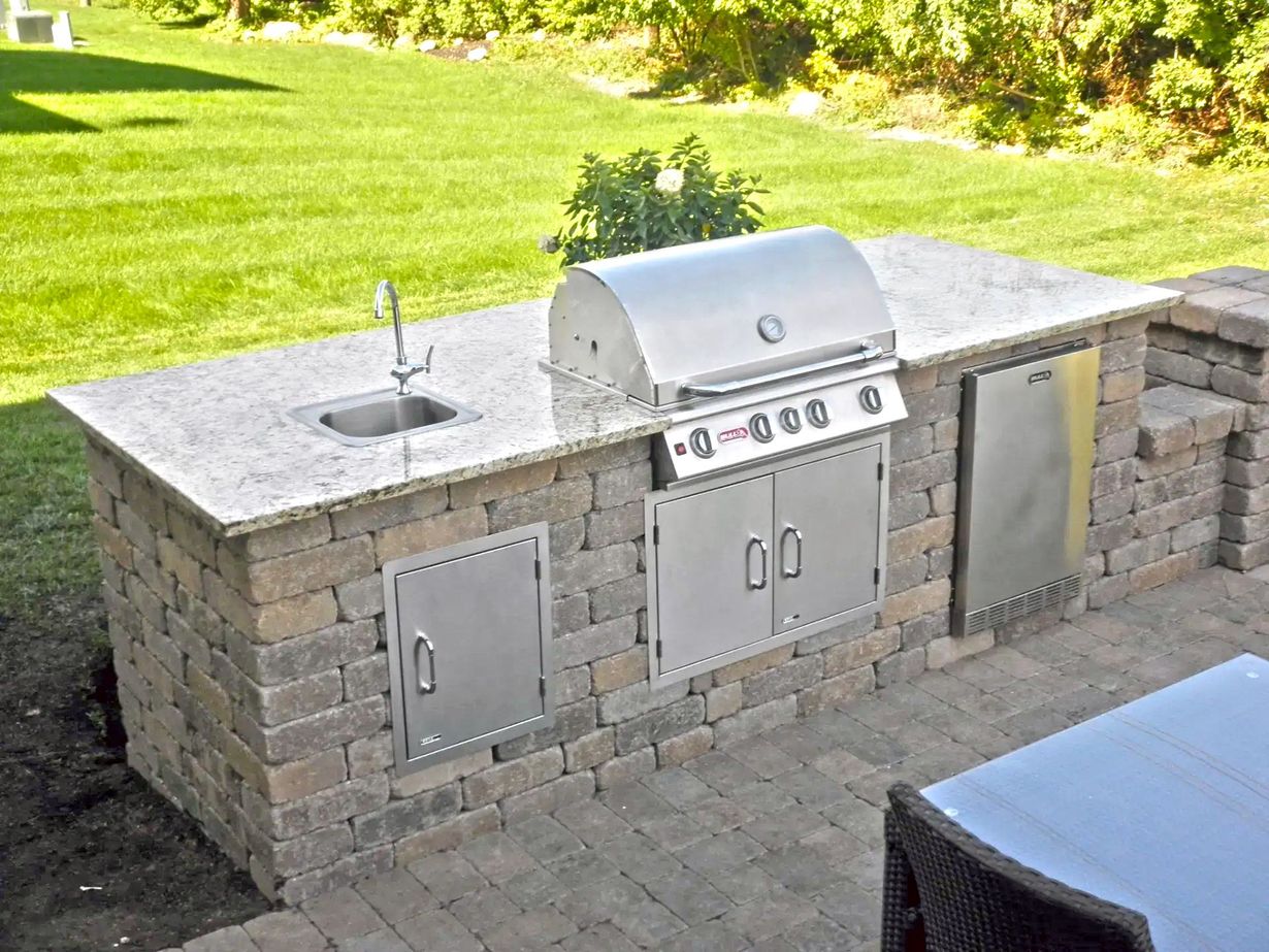 Outdoor bar with a granite countertop and sink, surrounded by plants, white seating, and a red sculpture. Ocean view in the background.