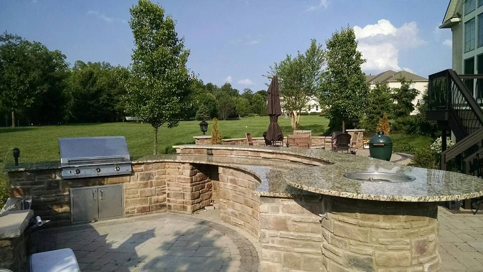 Outdoor kitchen with grill, granite countertop, stone facade, overlooking green lawn and trees.