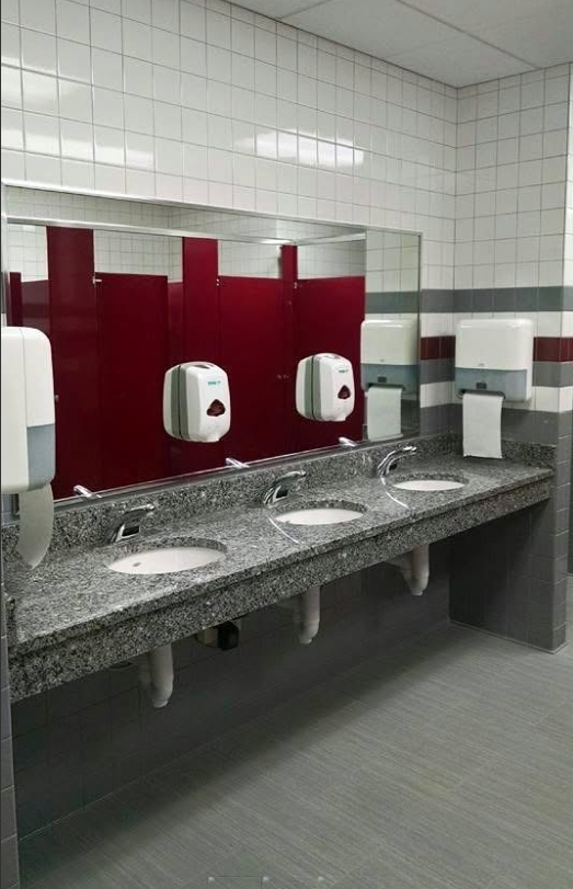 Public restroom with gray countertops, red dividers, white sinks and walls.