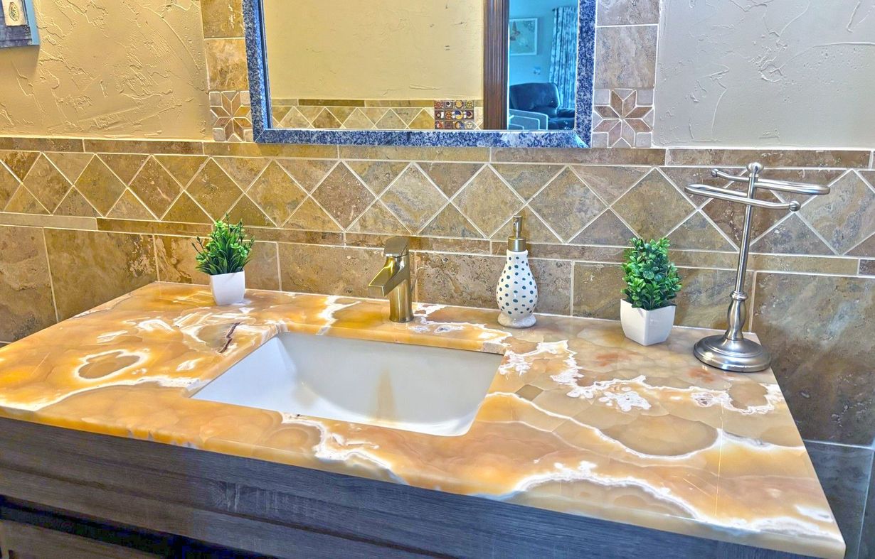 A bathroom with a white double vanity and a gray and white granite countertop. Two mirrors hang above the sinks.