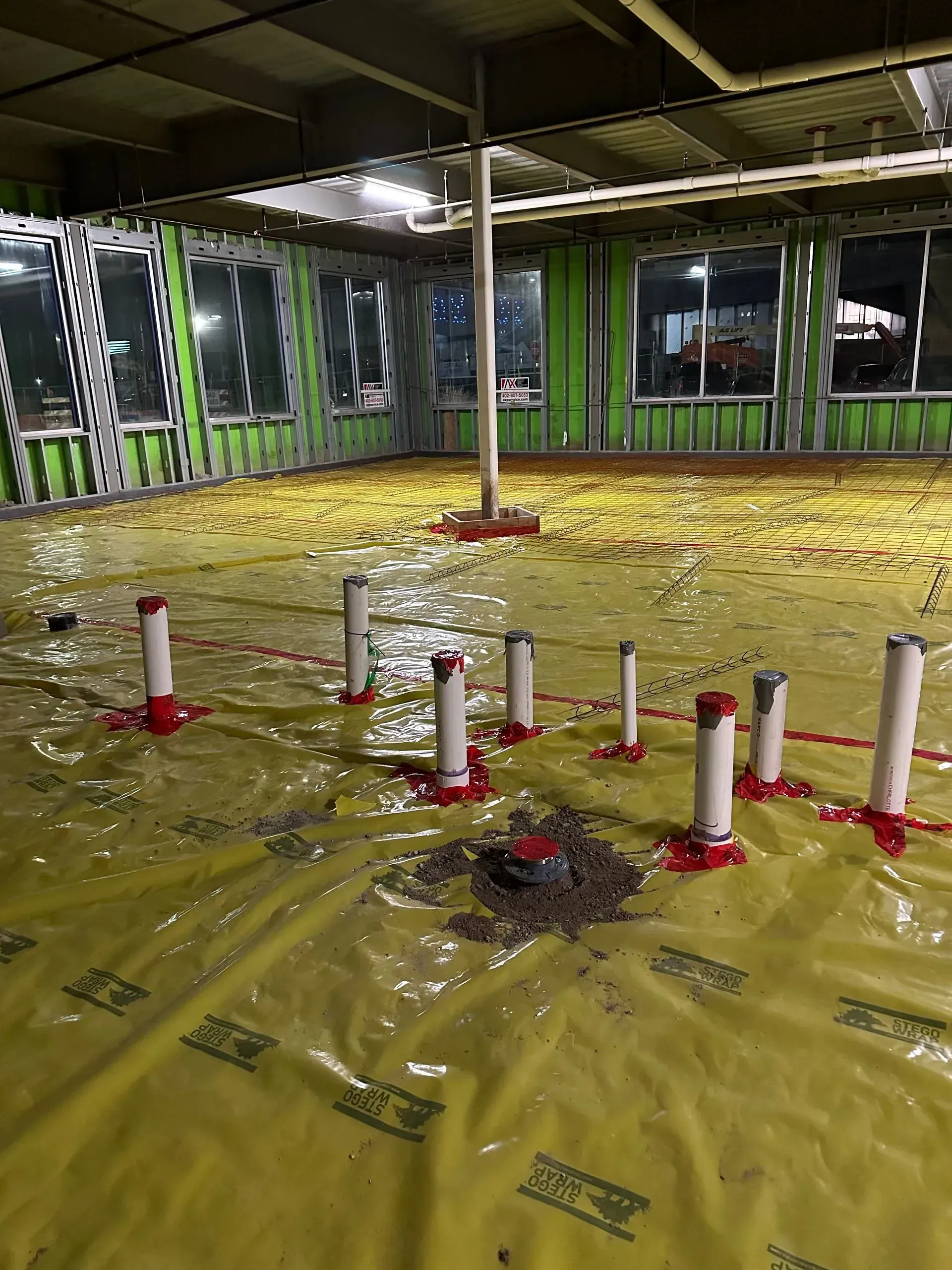 Interior construction site with plumbing and yellow vapor barrier on the floor.