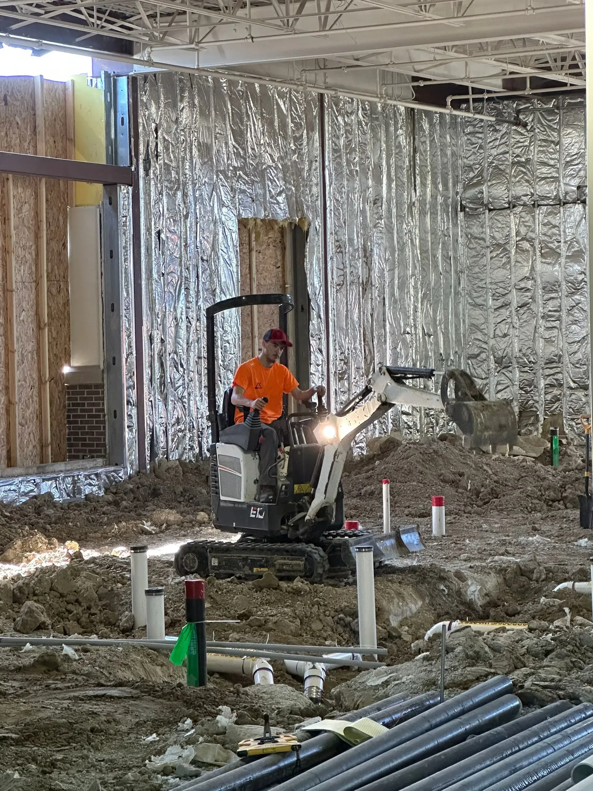 Construction worker operating a small excavator inside a building under construction.