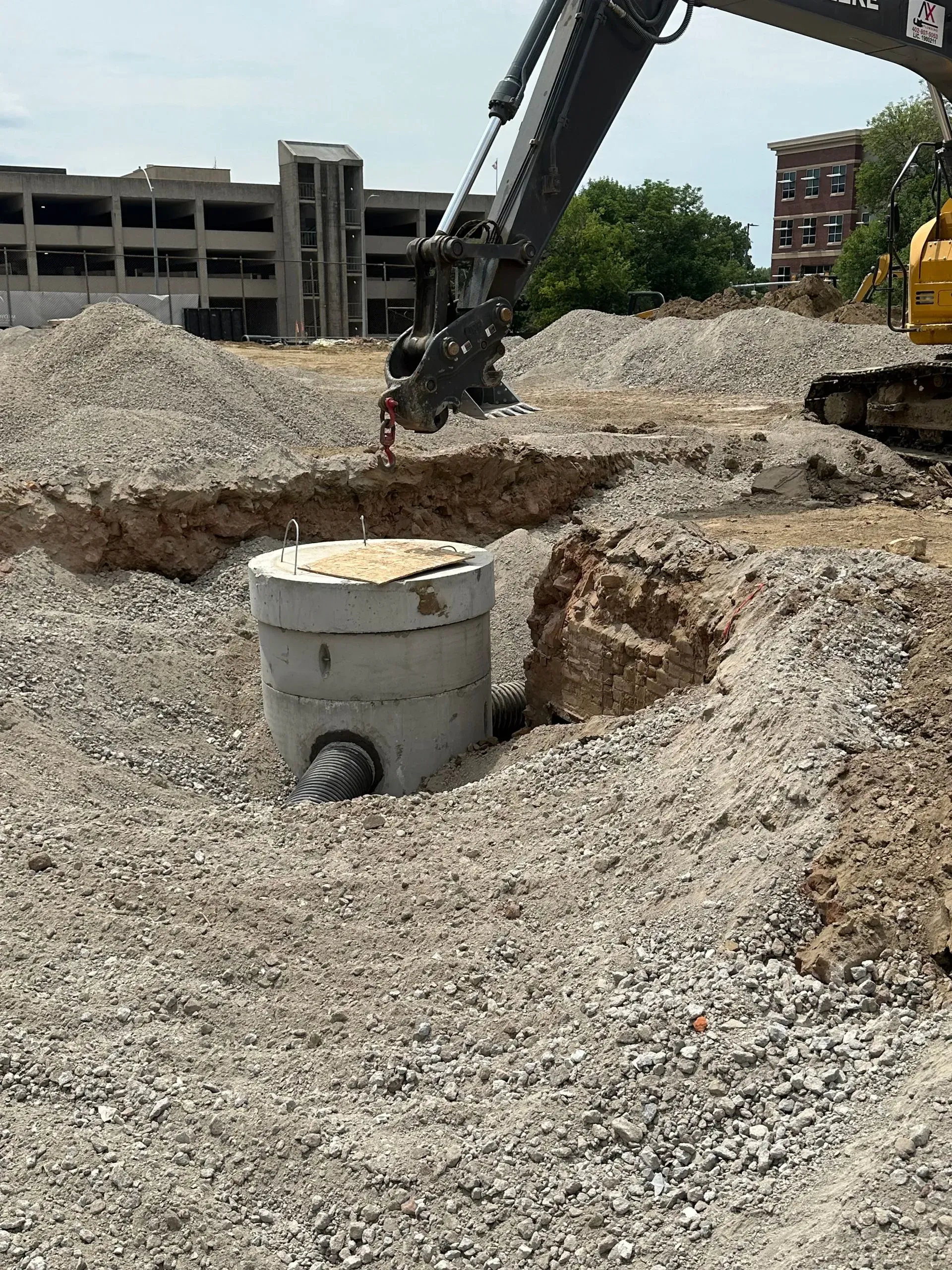 Excavator placing a concrete drainage structure in a construction site.