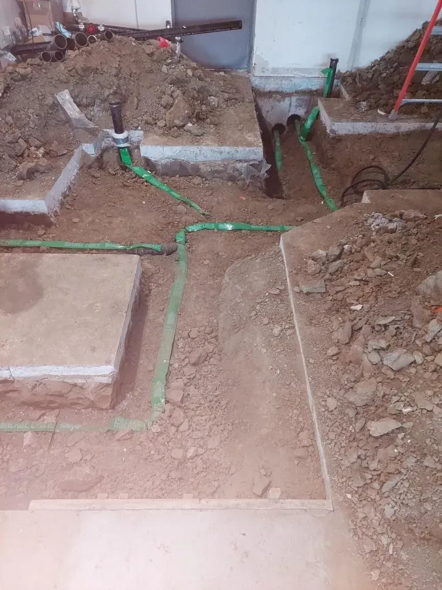 Green plumbing pipes in trenches dug into dirt during construction.