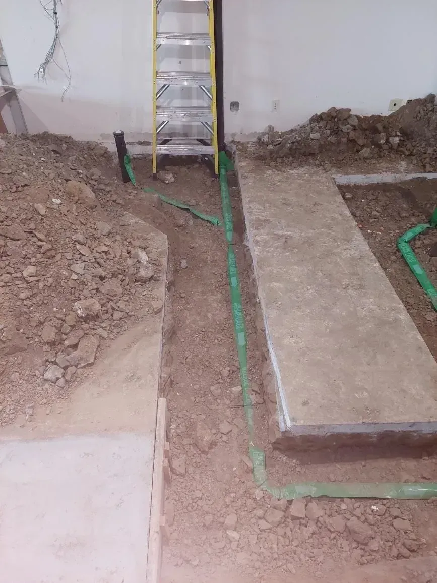 Construction site: Green pipes in trenches. Concrete blocks, dirt, and a ladder are visible.