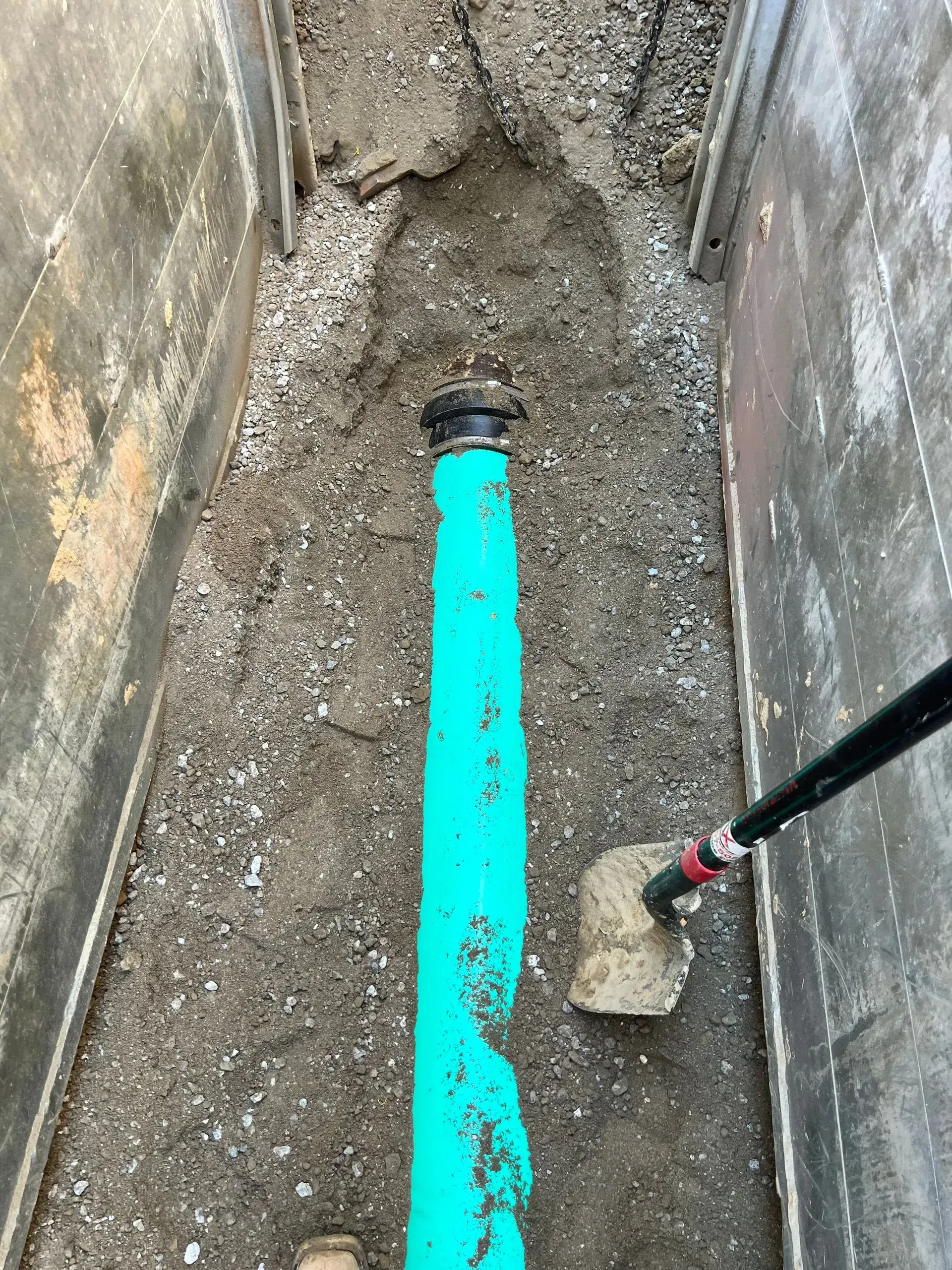 Blue pipe in trench with shovel and soil.