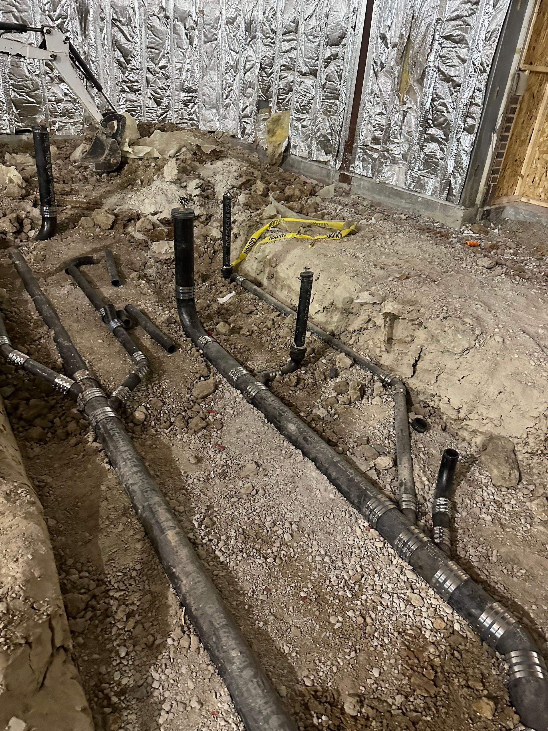 Underground plumbing pipes in a construction site, surrounded by gravel and soil.