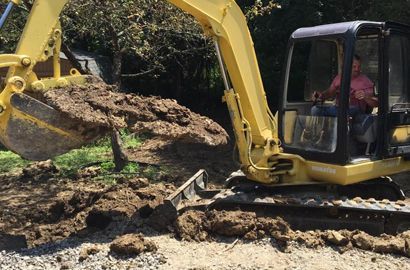A man is driving a yellow excavator in a dirt field.