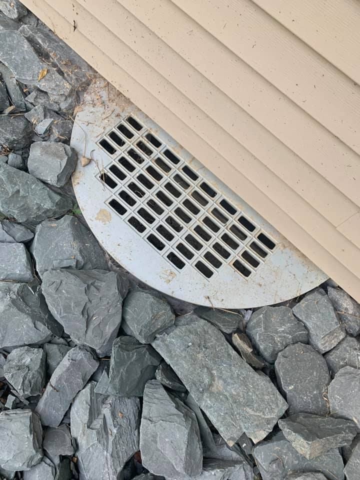 A drain cover is sitting on top of a pile of rocks next to a house.