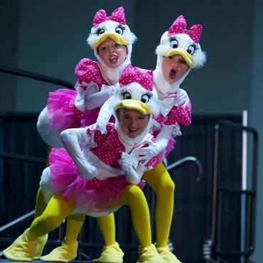 A group of young girls in pink and yellow tutus are dancing on a stage.