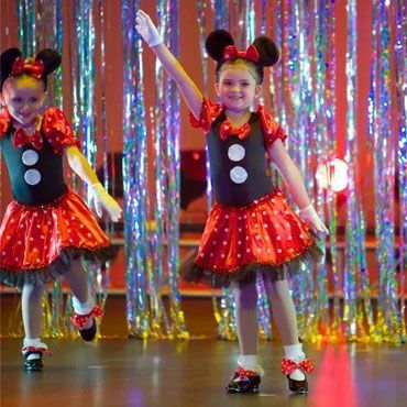Two little girls in minnie mouse costumes are dancing on a stage.