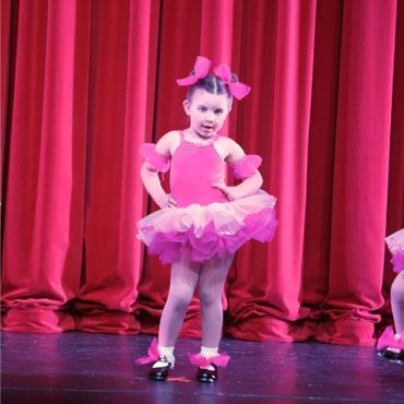 A little girl in a pink tutu is dancing on a stage.