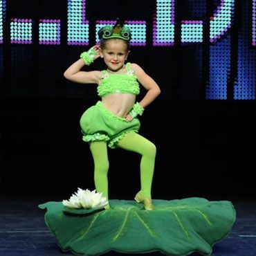 A little girl in a green dress dancing on a stage.