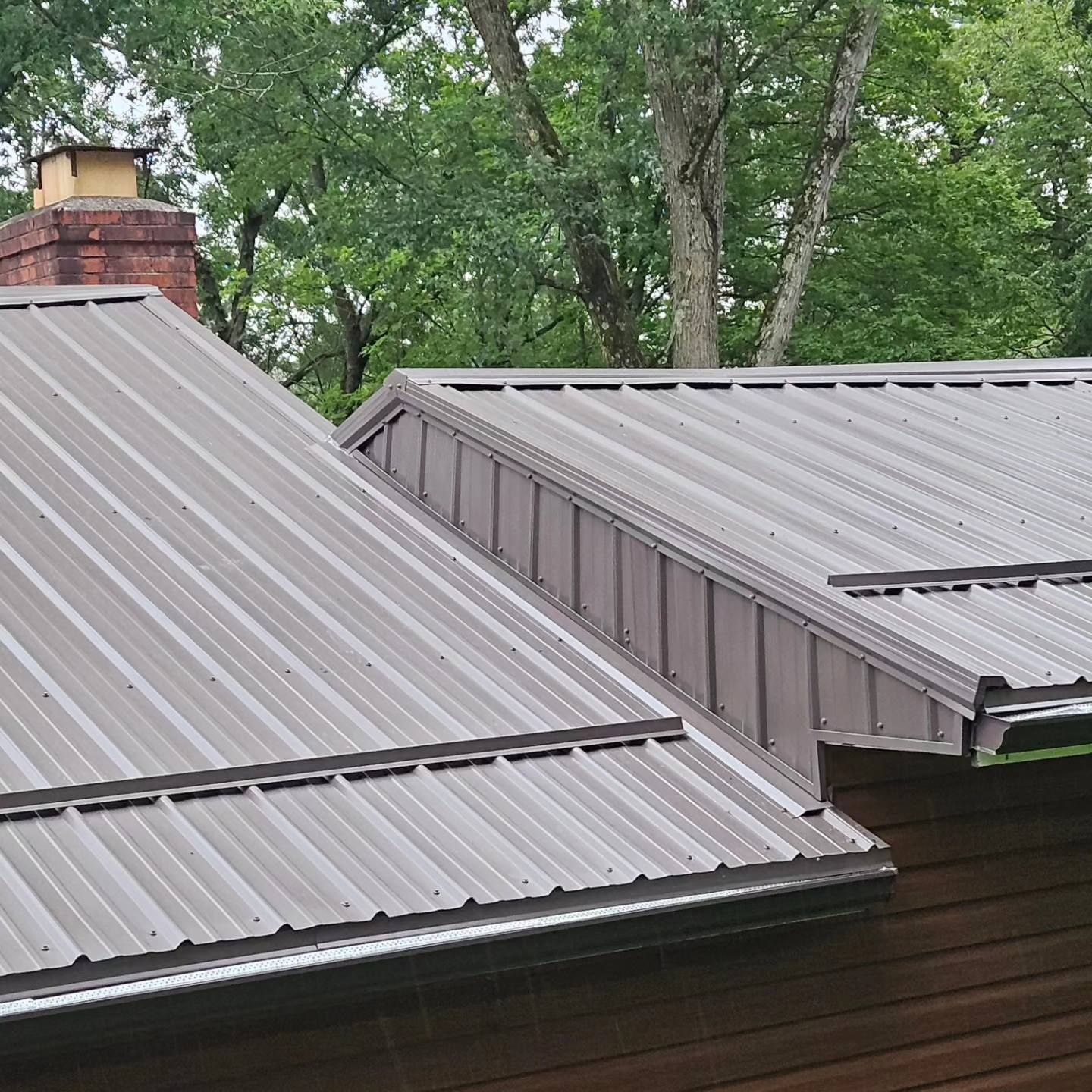 A close up of a metal roof on a house with trees in the background.