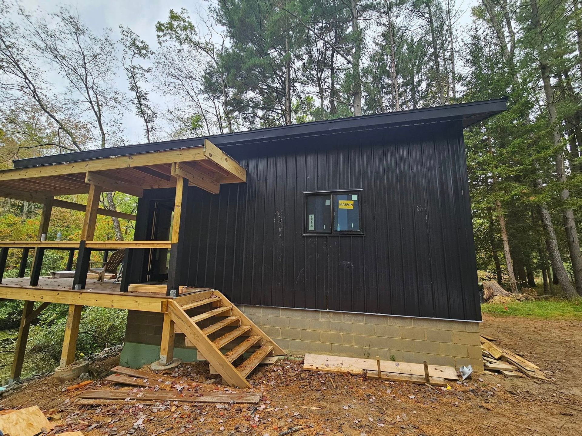 A small black house with a wooden deck and stairs in the woods.