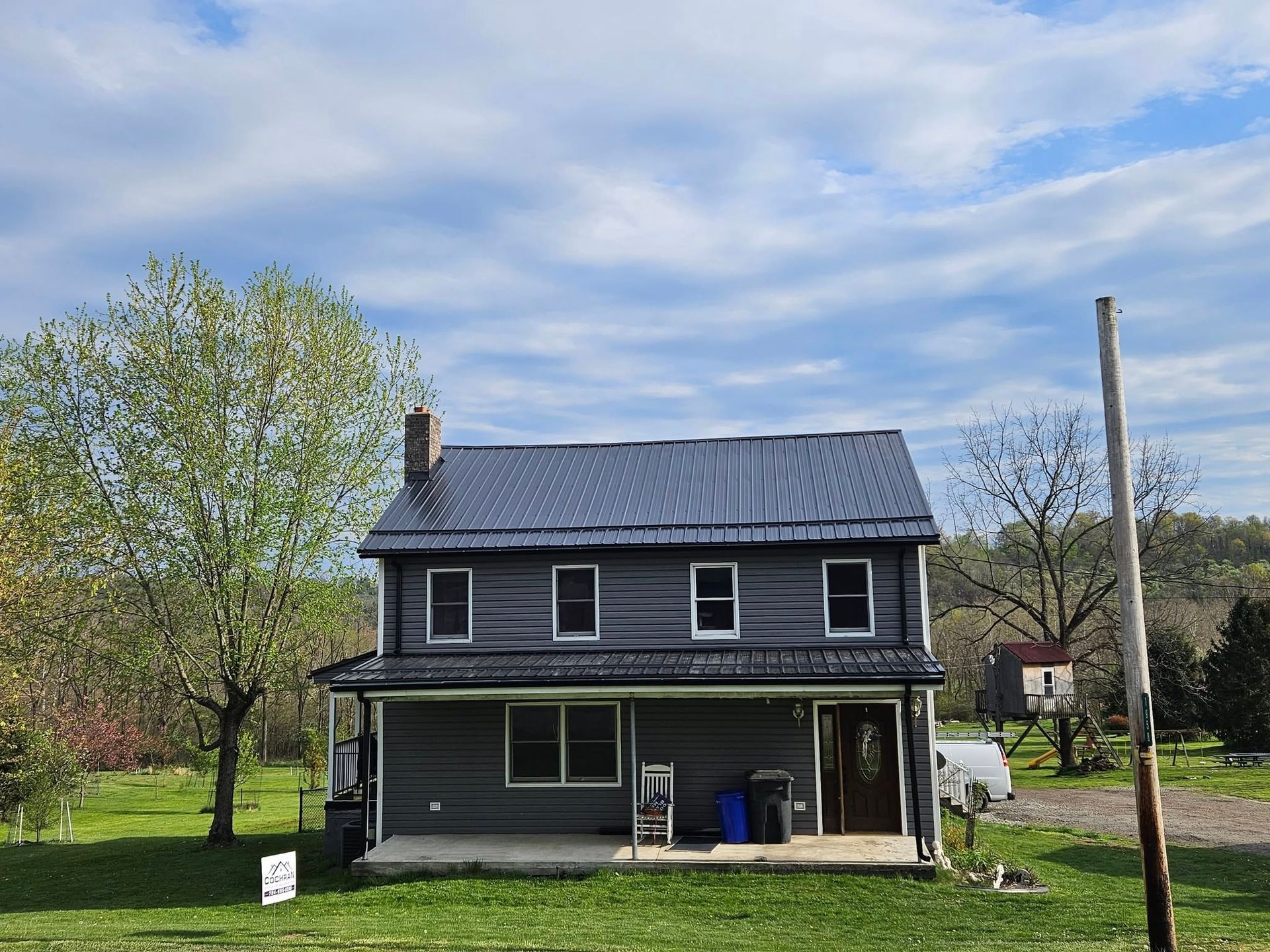 A large house with a metal roof is sitting on top of a lush green field.