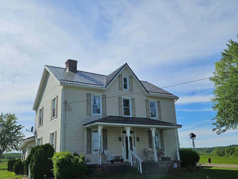 A large white house with a porch in the middle of a field.