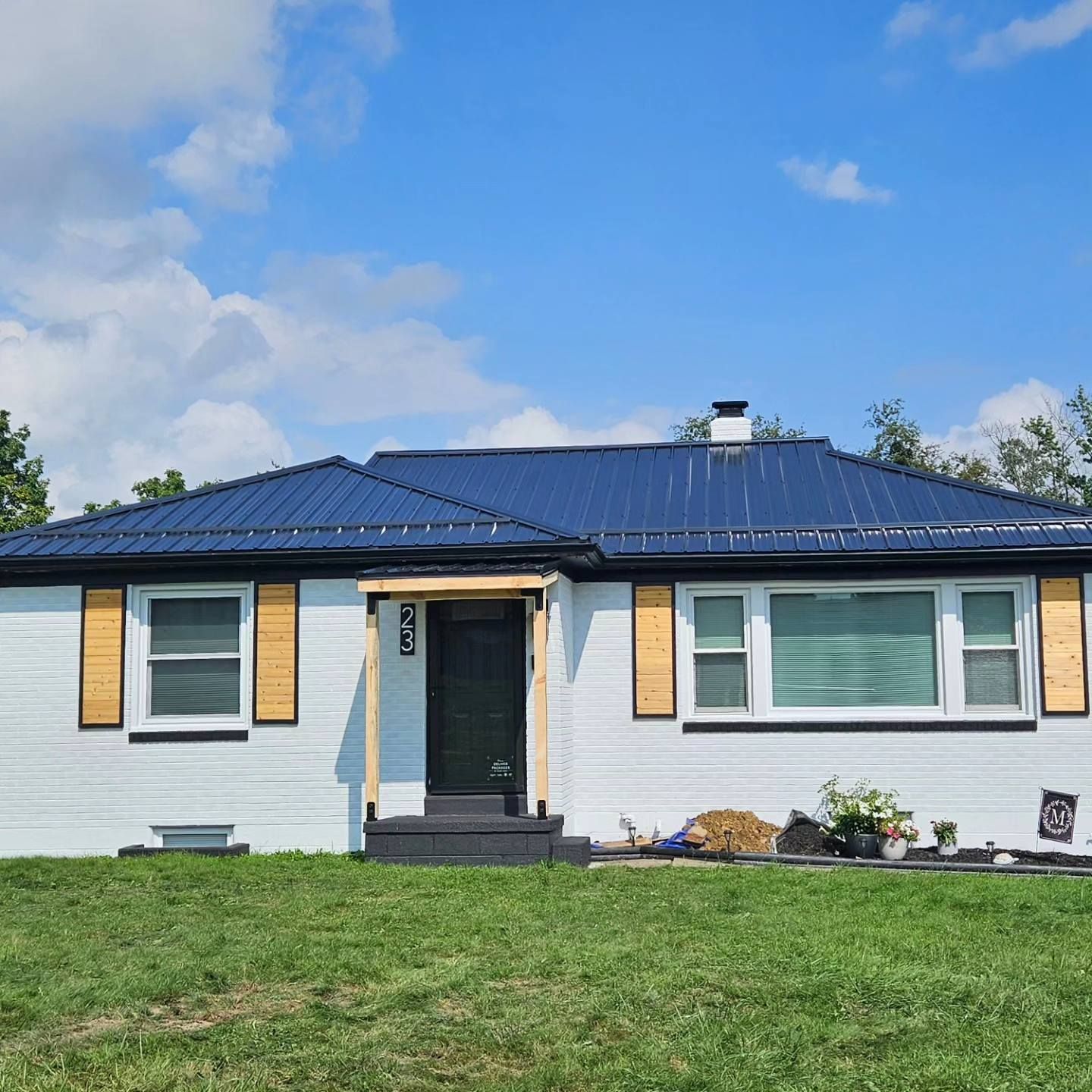 A white house with a blue roof and wooden shutters is sitting on top of a lush green field.