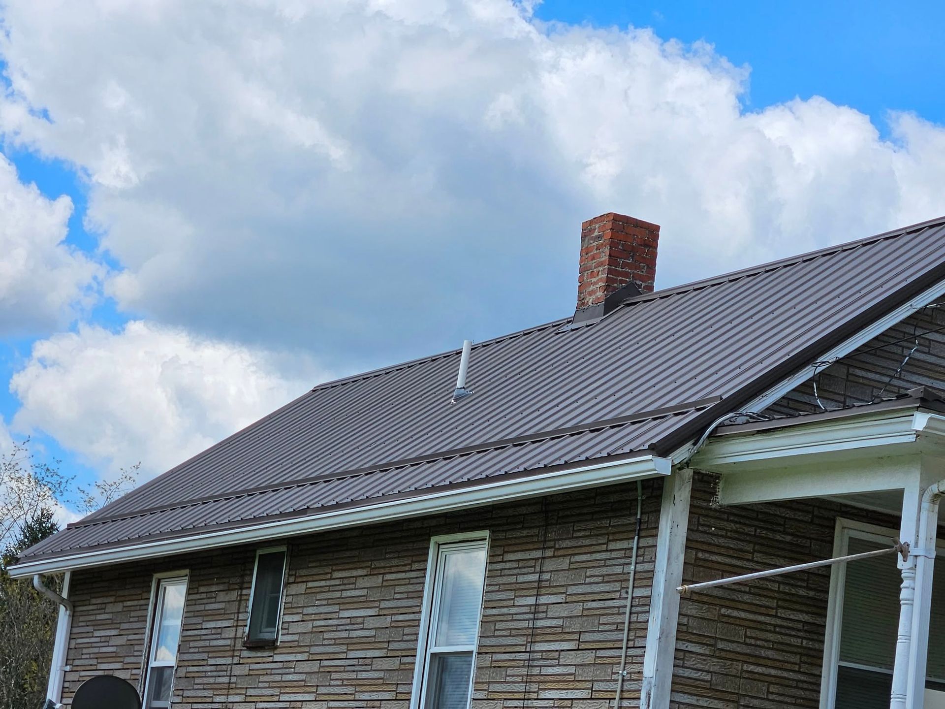 A brick house with a brown roof and a chimney on top of it.