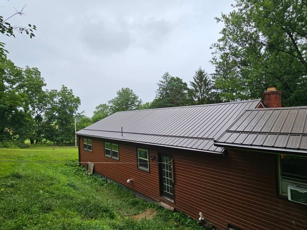 A brick house with a metal roof is sitting in the middle of a grassy field.