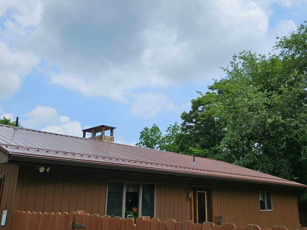 A brown house with a metal roof and a wooden fence