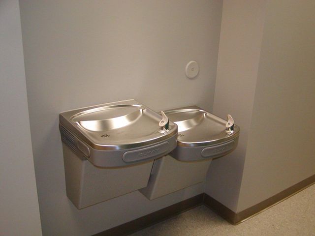 Two stainless steel water fountains on a wall in a bathroom