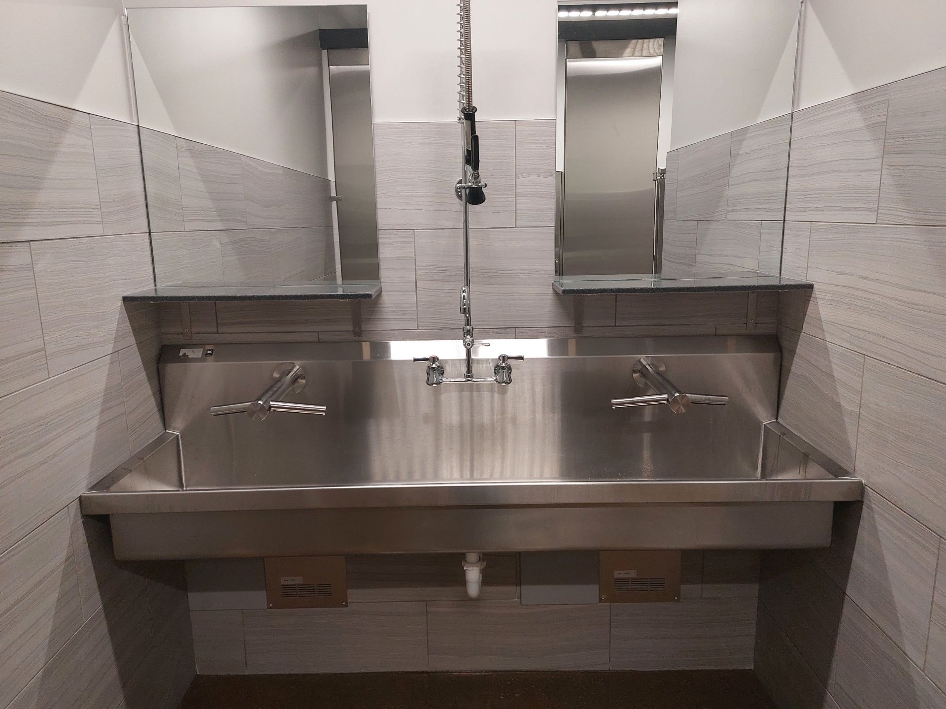 A bathroom with a stainless steel sink and two mirrors