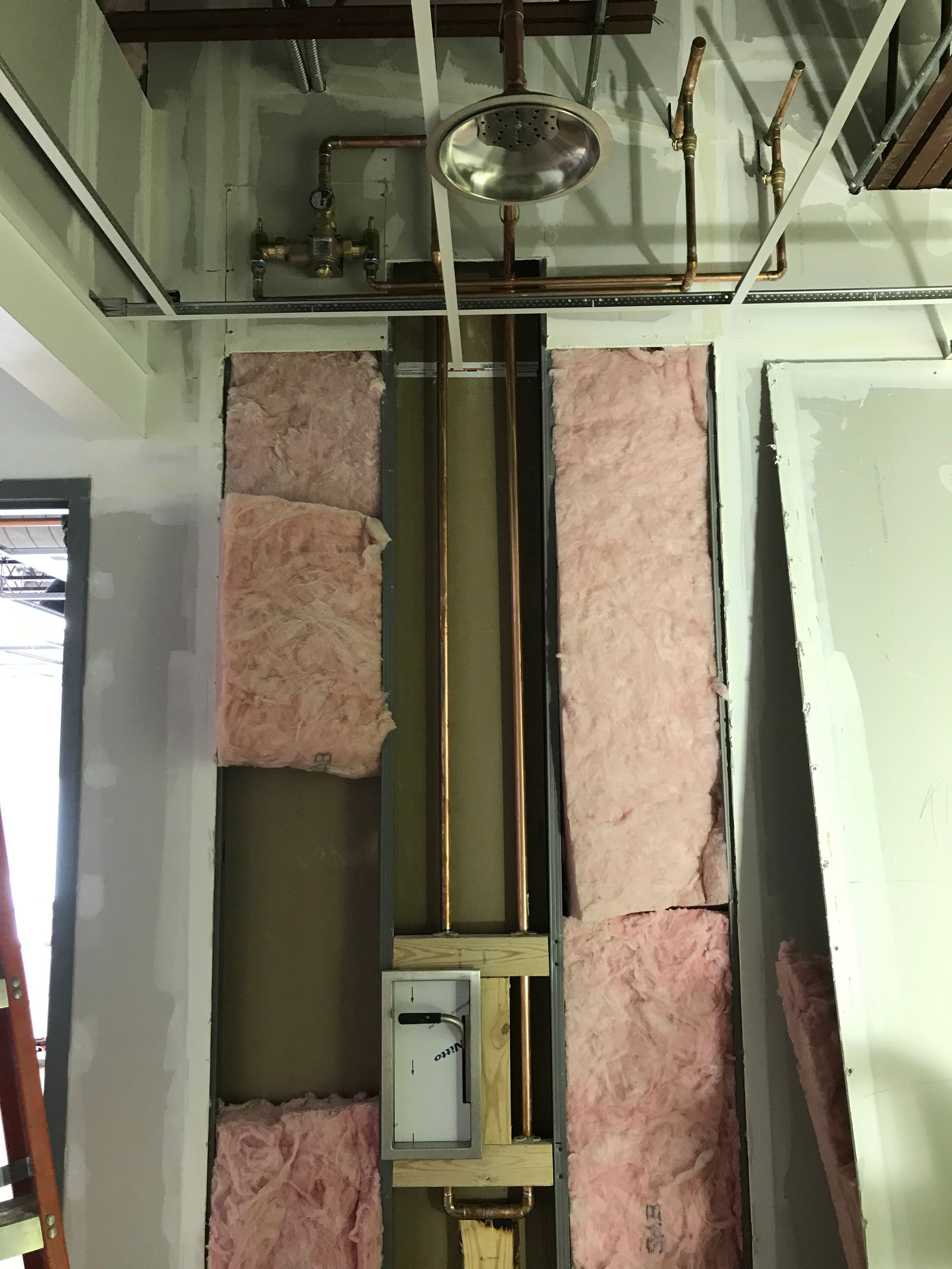 A room with pink insulation and copper pipes coming out of the ceiling.