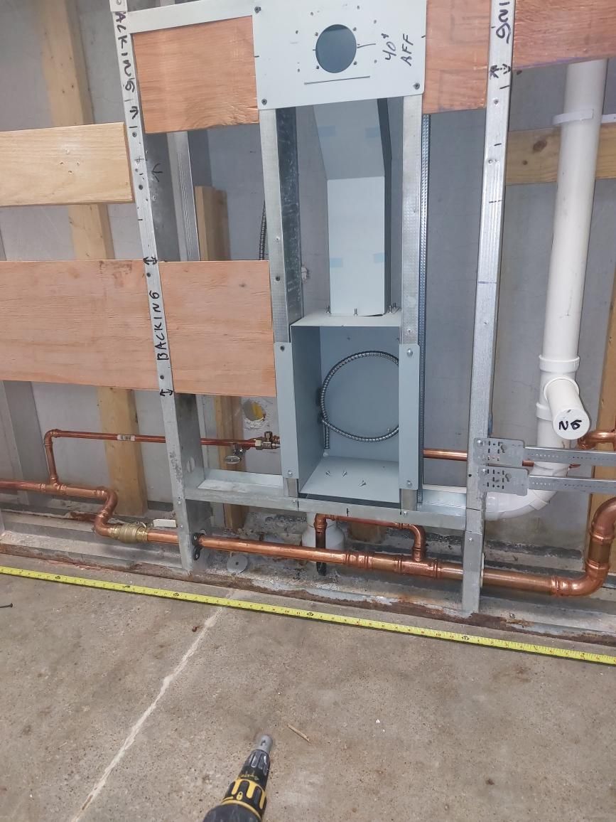 A person is working on a wall with pipes and a drill.