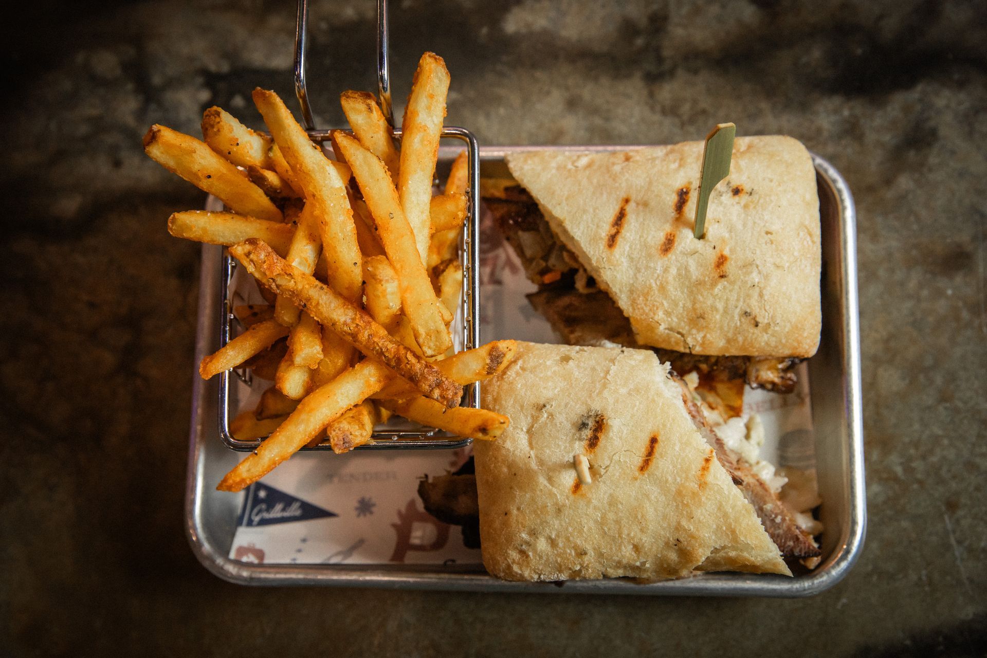 Sandwich and fries on a tray. The sandwich is cut in half with a toothpick. Fries are to the left.