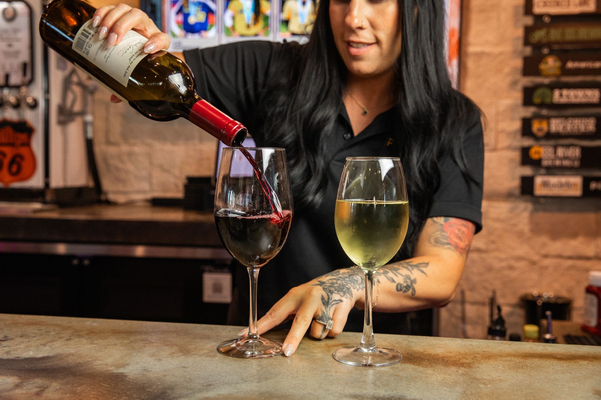 Woman pouring red wine into a glass, with a glass of white wine beside it on a bar.