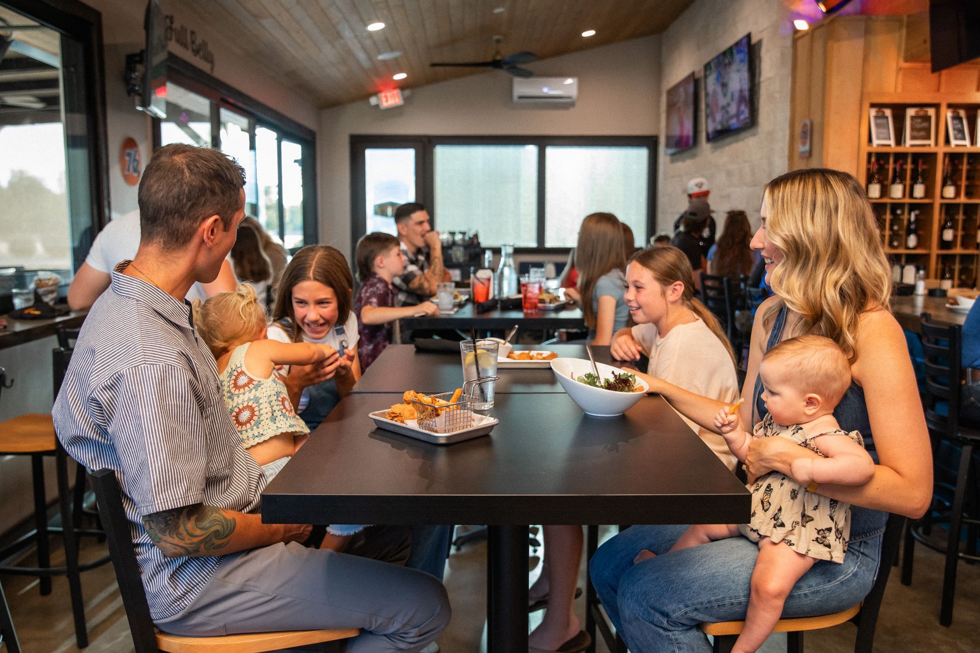 Family dining at a restaurant; parents and children seated at a table, enjoying food and drinks, inside setting.