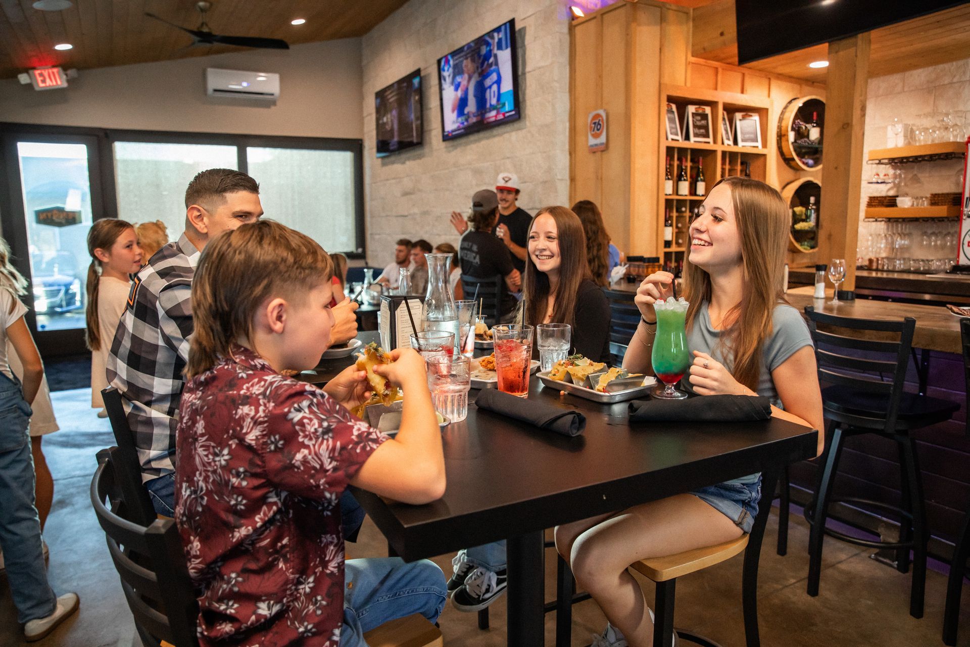 People laughing and eating at a restaurant. Boy with a mullet is eating, girl is drinking a green drink.