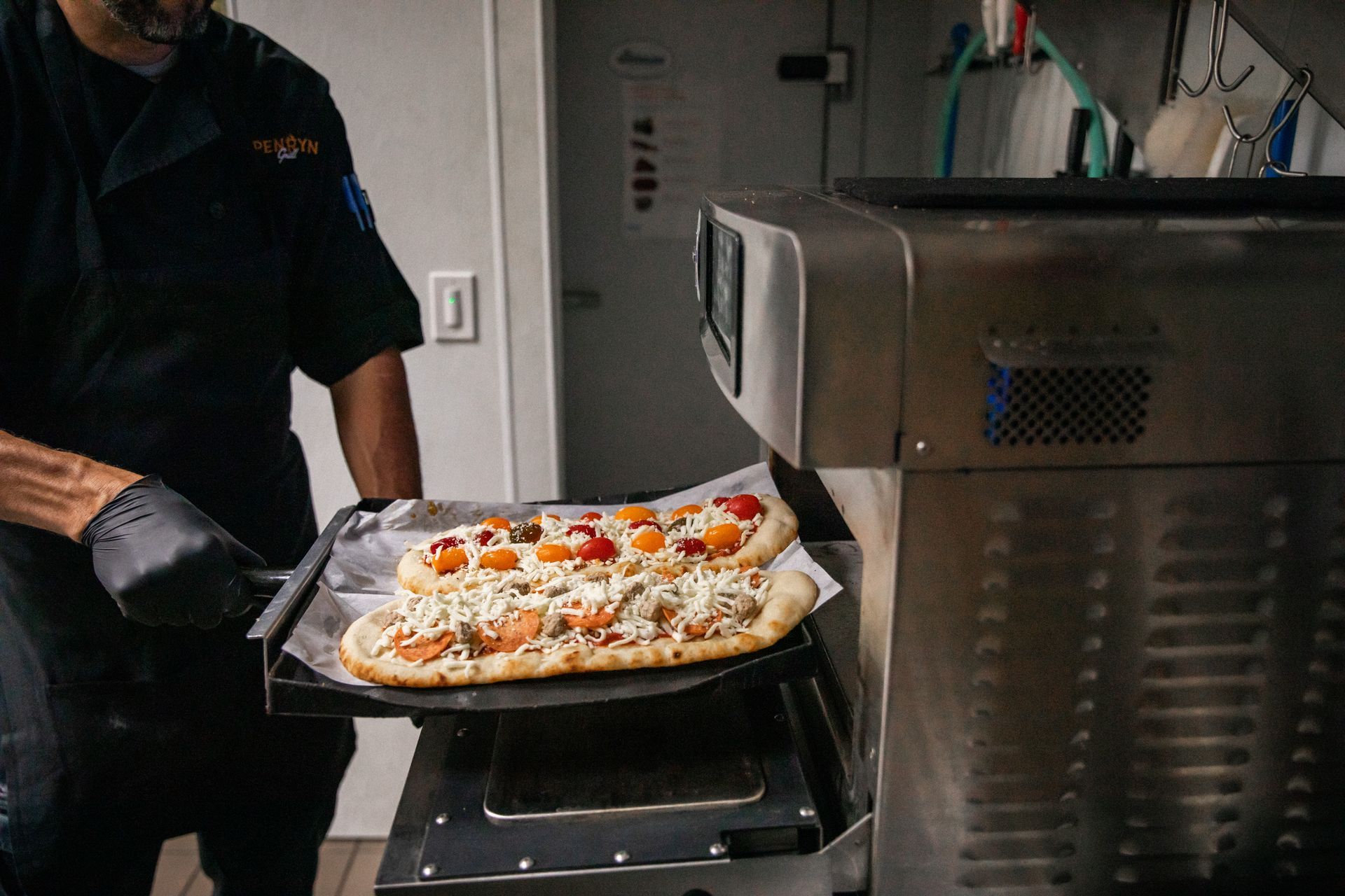 Chef placing two pizzas with toppings into a metal oven.