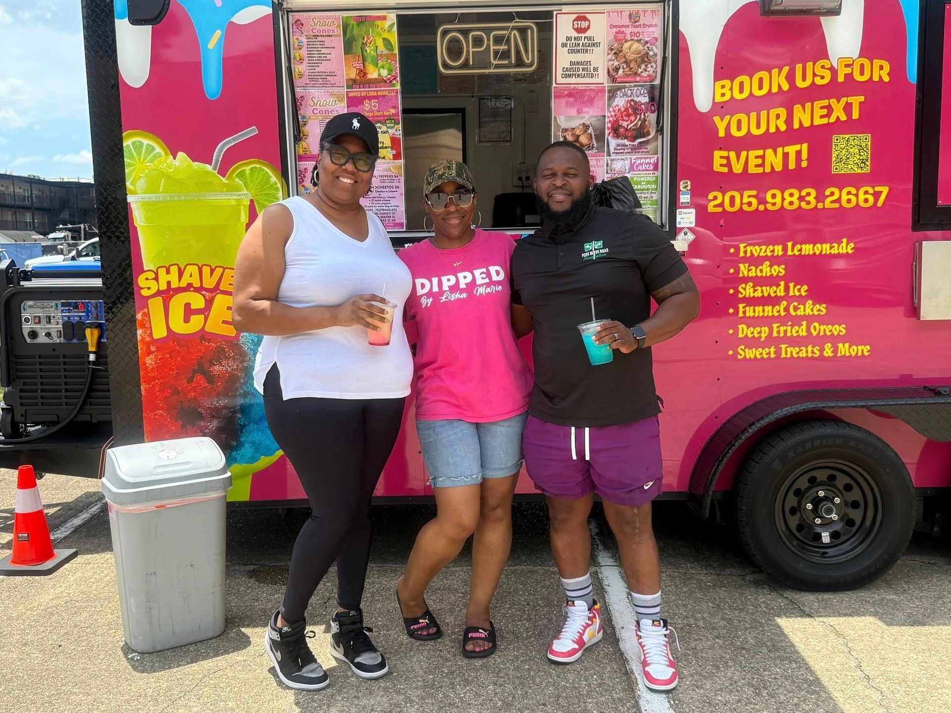 Three people pose in front of a pink food truck that has 