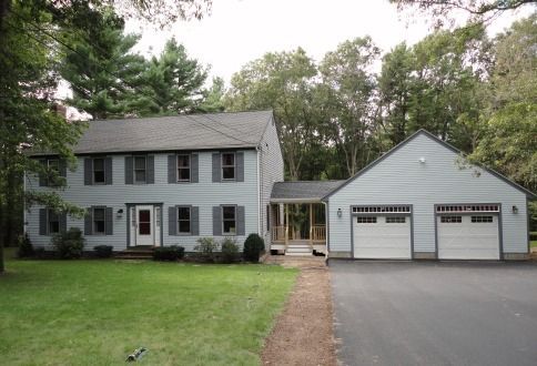 A two-story grey colonial house with a matching detached garage connected by a covered walkway, set on a grassy lot.