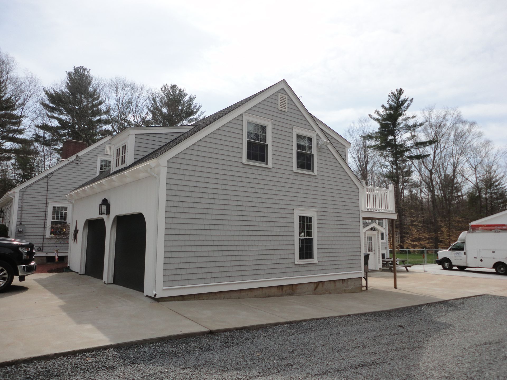 A side view of a gray-sided house with an attached two-car garage, white trim, and a concrete driveway.