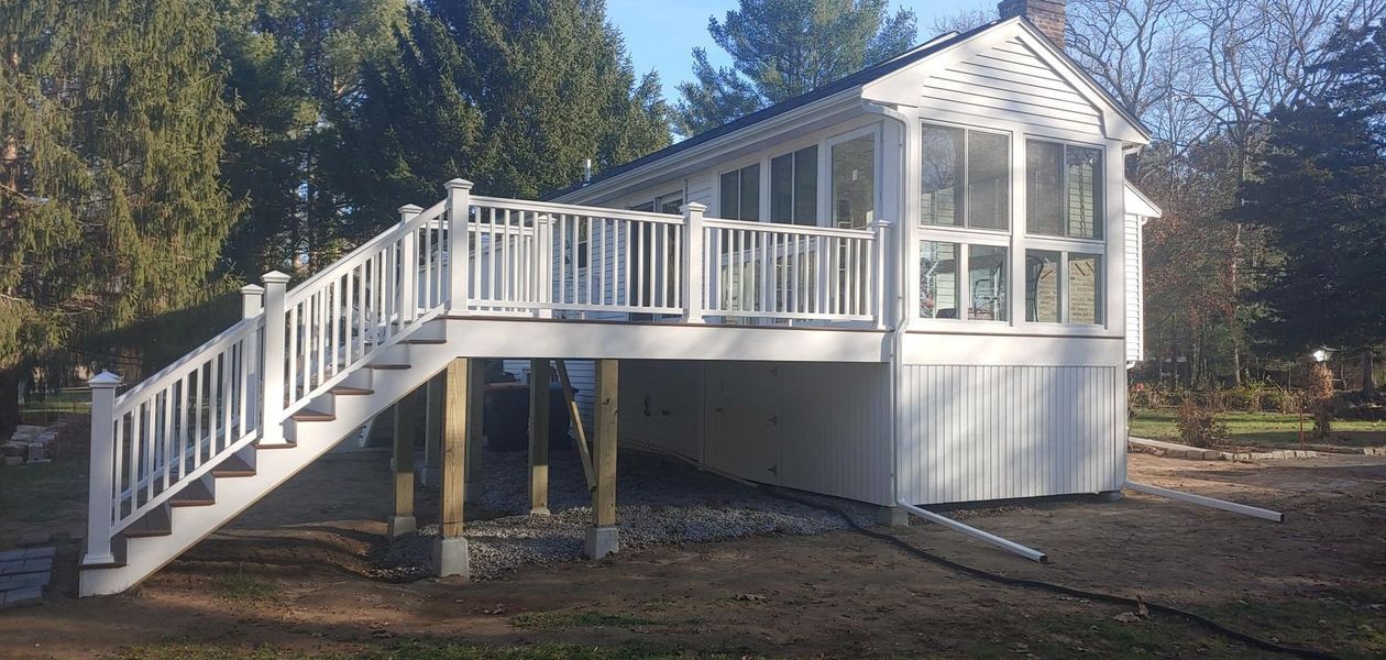White deck and stairs leading to a sunroom with a clear, sunny sky.