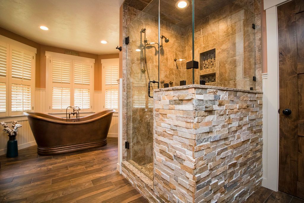 A stone shower with a built-in seat, set against wood paneled double doors and a wood floor in a bathroom.