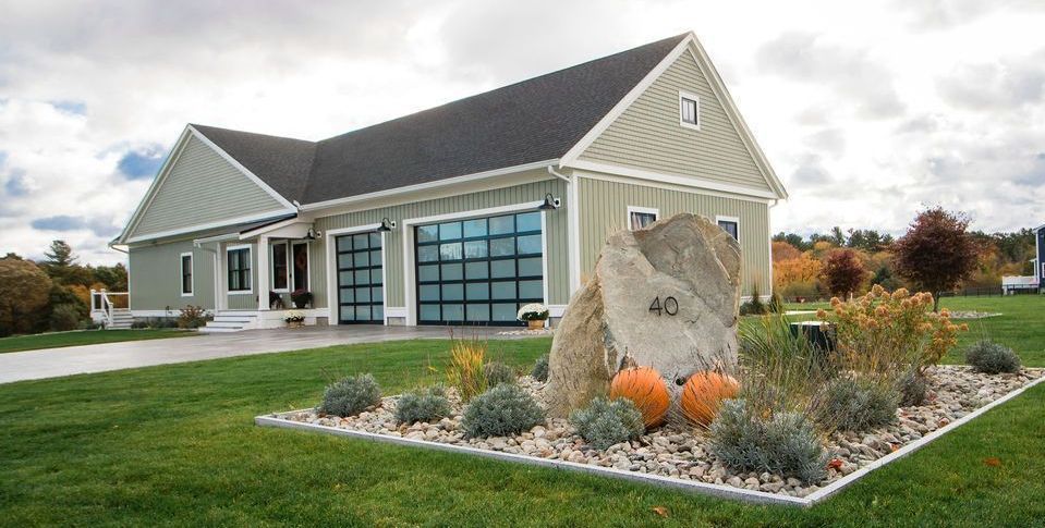 Green house with glass garage doors, rock with pumpkins, and manicured yard.