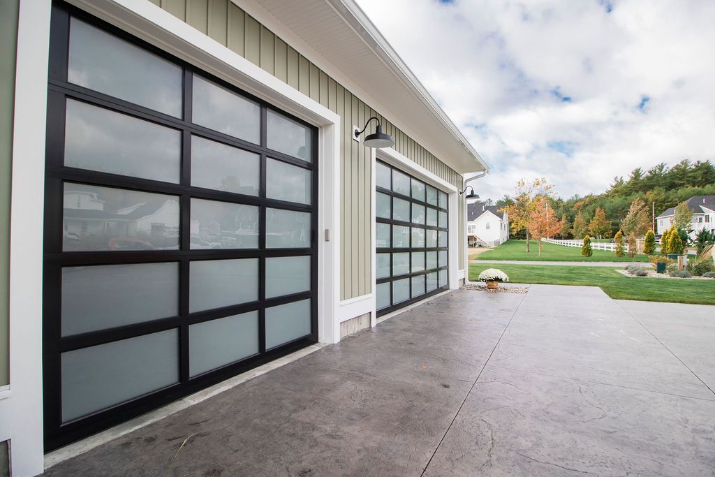 A modern garage with two black-framed frosted glass doors, set against a house with light vertical siding and a driveway.