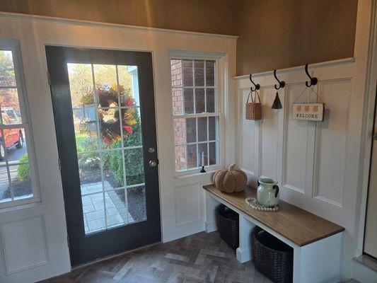 Entryway with black door, white paneling, bench, and fall decorations.
