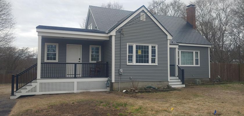 Gray house with porch and chimney on an overcast day.
