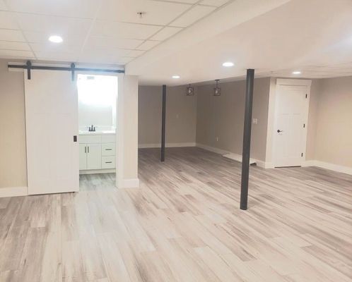 Finished basement with light wood floors, white walls, and sliding barn door to a bathroom.