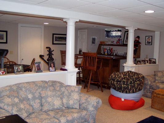 Basement living area with sofa, bar, beanbag chairs, and support columns.