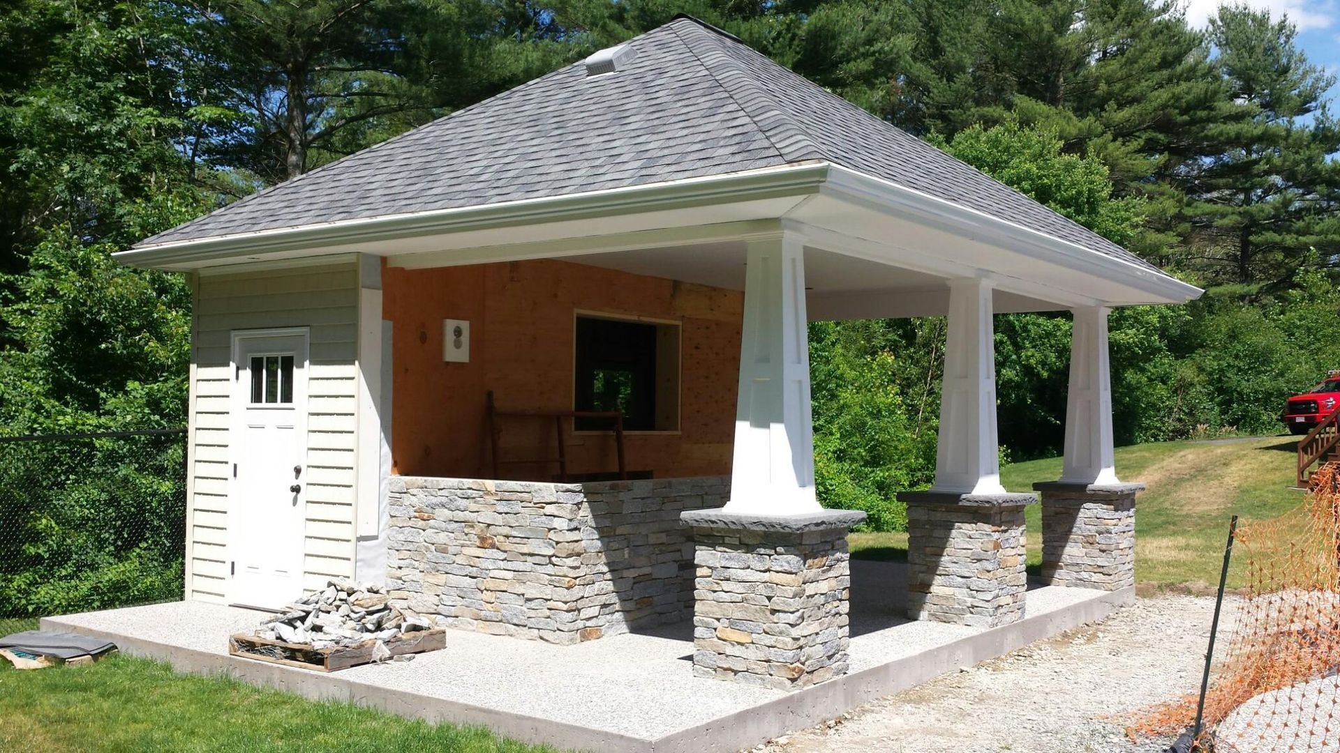 Pavilion with stone base, white columns, grey roof, and a small building with a white door.