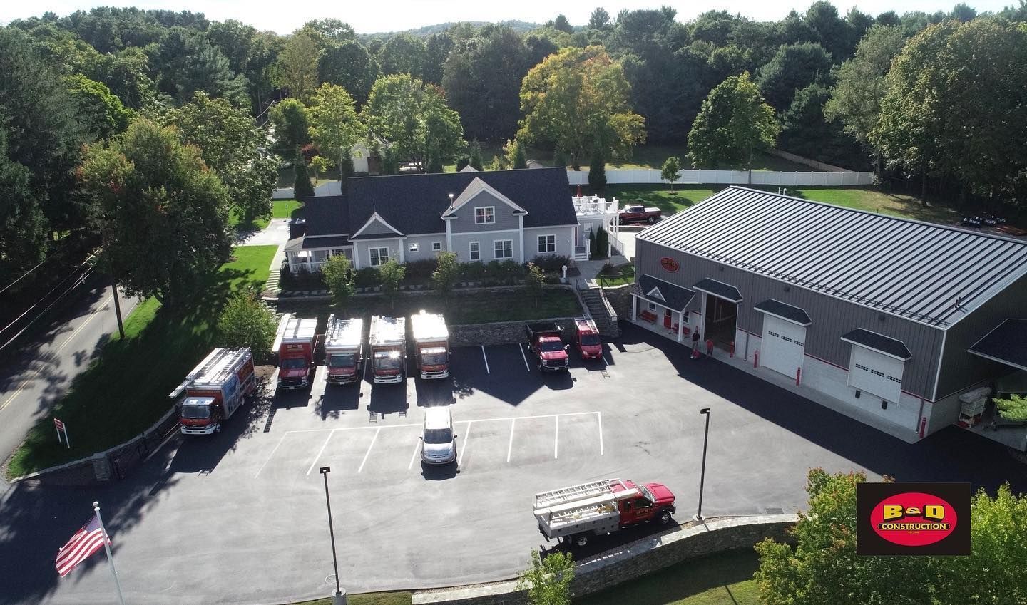 Fire station with fire trucks parked outside, surrounded by trees, and a light-colored building.