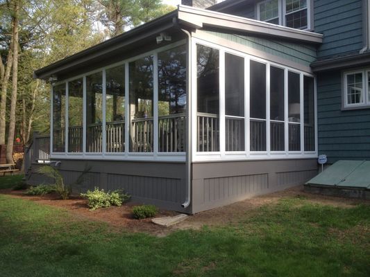 Screened-in porch attached to a house with dark gray siding, white trim, and green grass.
