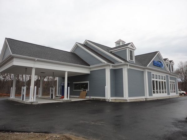Bank building with blue siding, white trim, and drive-up lanes on a gray day.