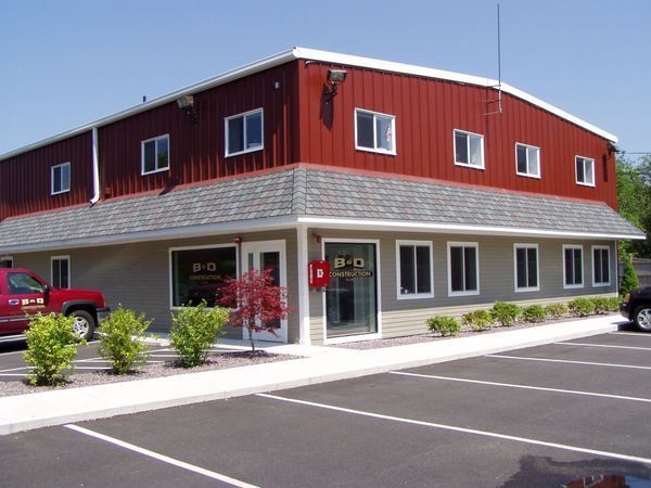 Red and tan two-story building with windows, a red SUV parked outside, and a small parking lot.